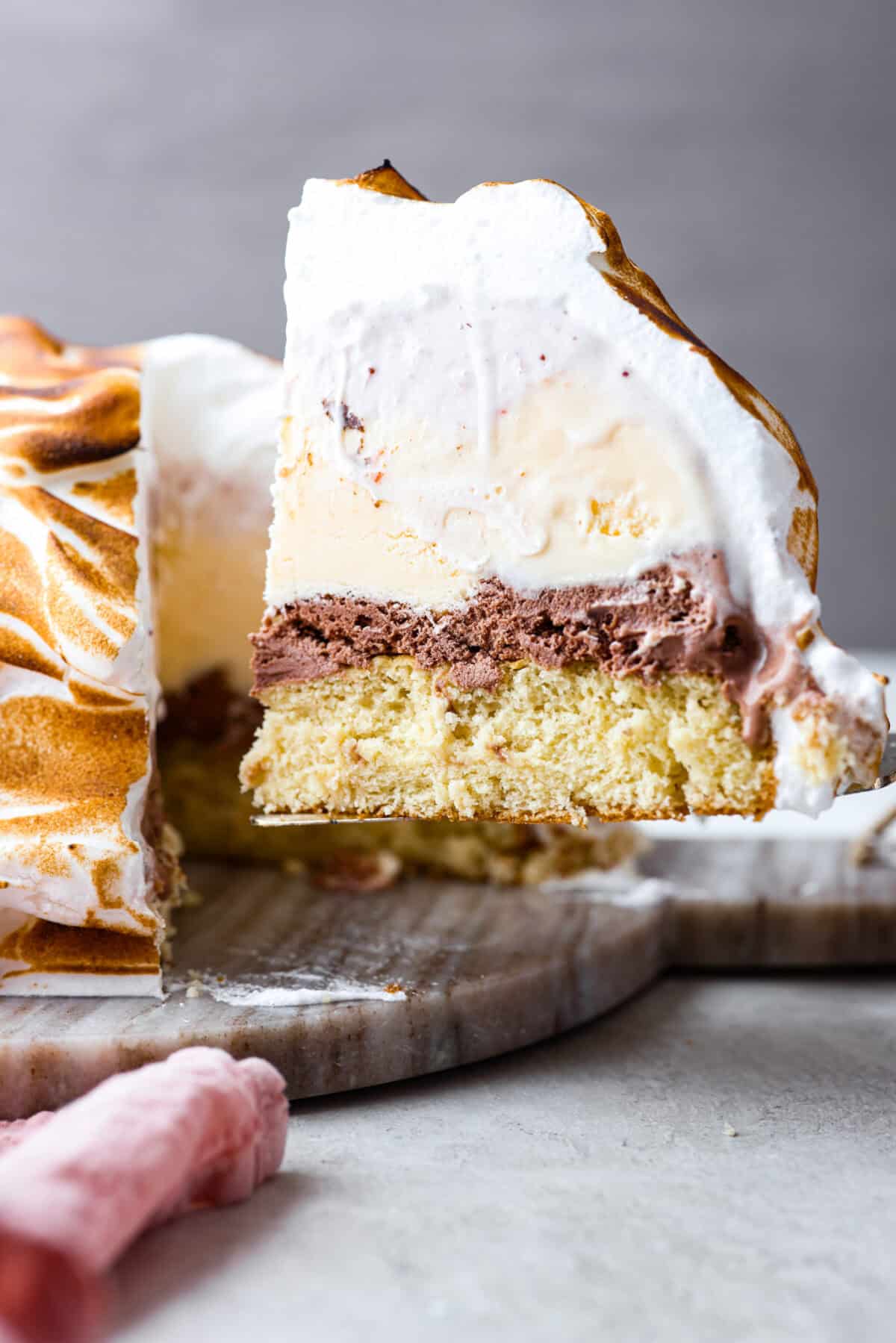 Side shot of slice of baked Alaska being served out of the whole cake. 