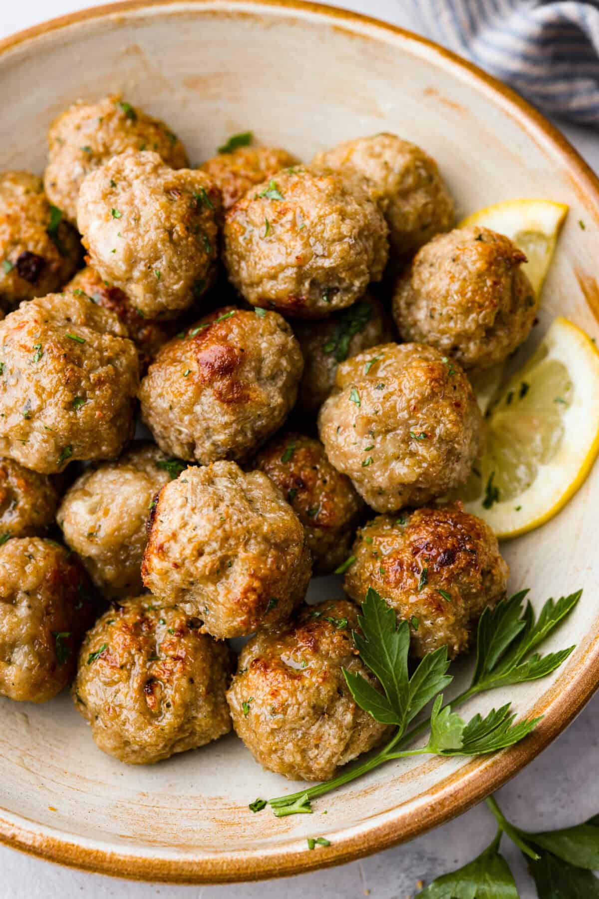 Close view of the meatballs served in a bowl garnished with parsley and lemon.