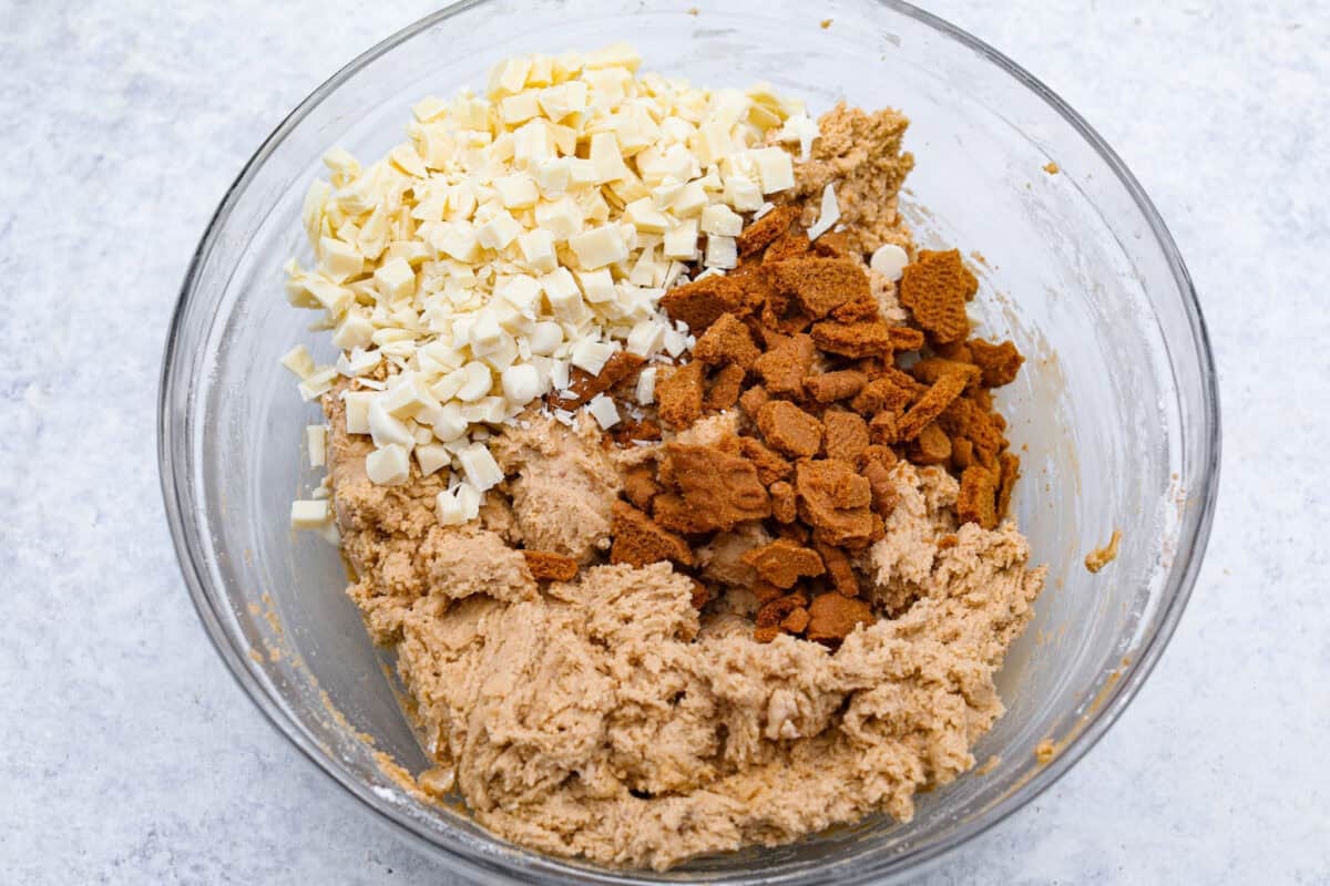 Overhead shot of bowl with Biscoff cookie bits, chunks of white chocolate over cookie dough. 