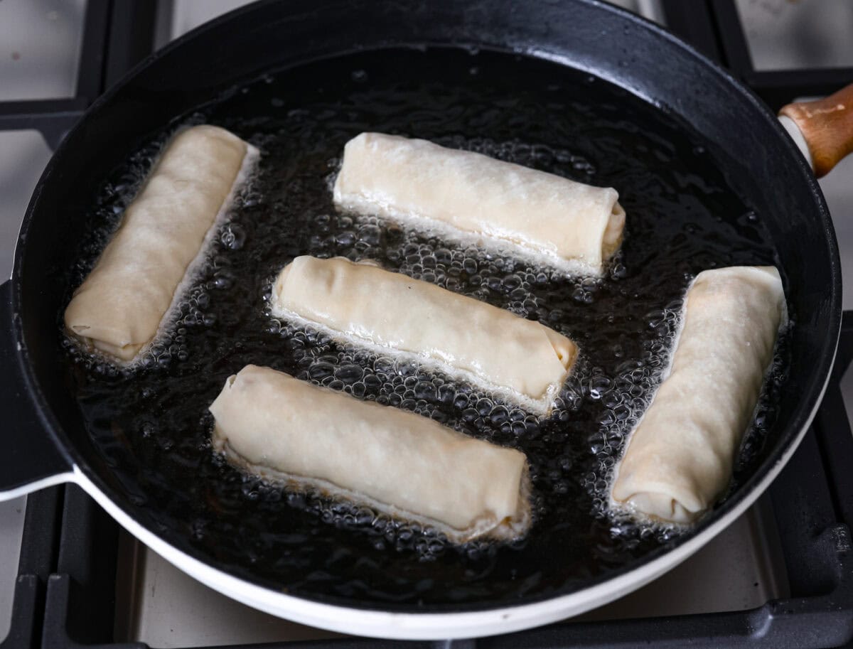 Overhead shot of 5 rolled breakfast egg rolls being fried in pan. 