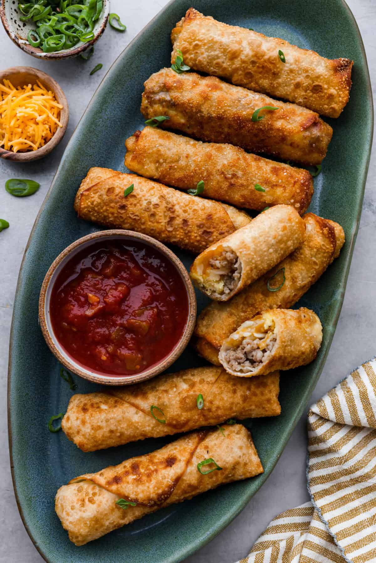 Overhead shot of a plate of cooked egg rolls with salsa in a bowl next to egg rolls. 