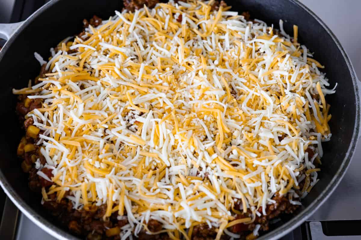 Angle shot of ground beef, beans, and Rotel mixture with cheese sprinkled over the top of the inside of cowboy cornbread casserole . 