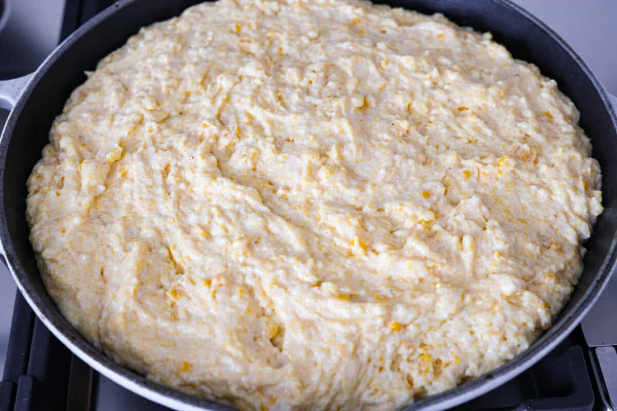 Overhead shot of cornbread batter spread over ground beef and cheese mixture. 