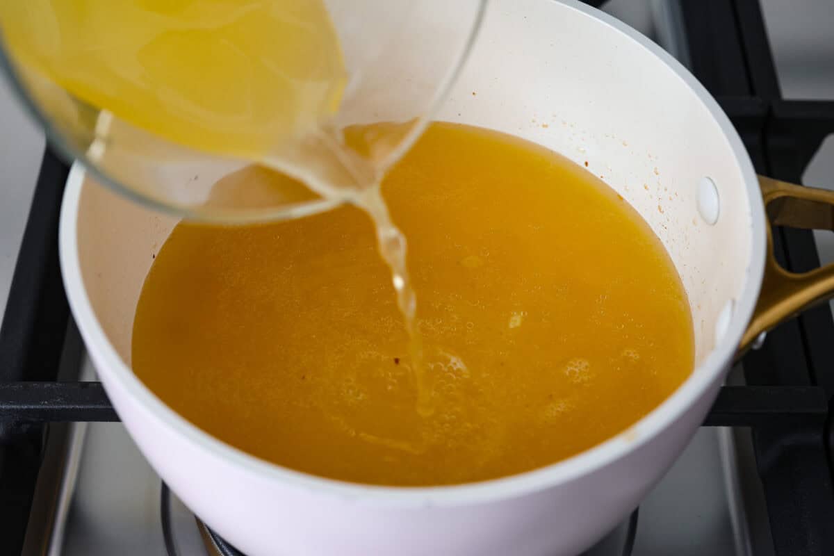 Overhead shot of someone pouring chicken broth into the onion, butter and garlic mixture. 