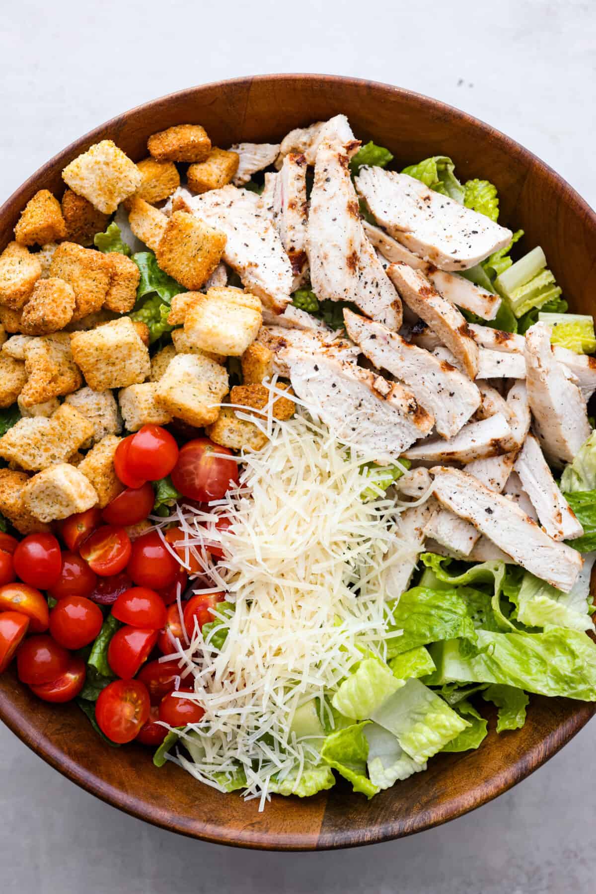 Grilled chicken caesar salad in a bowl. ready to be mixed. 