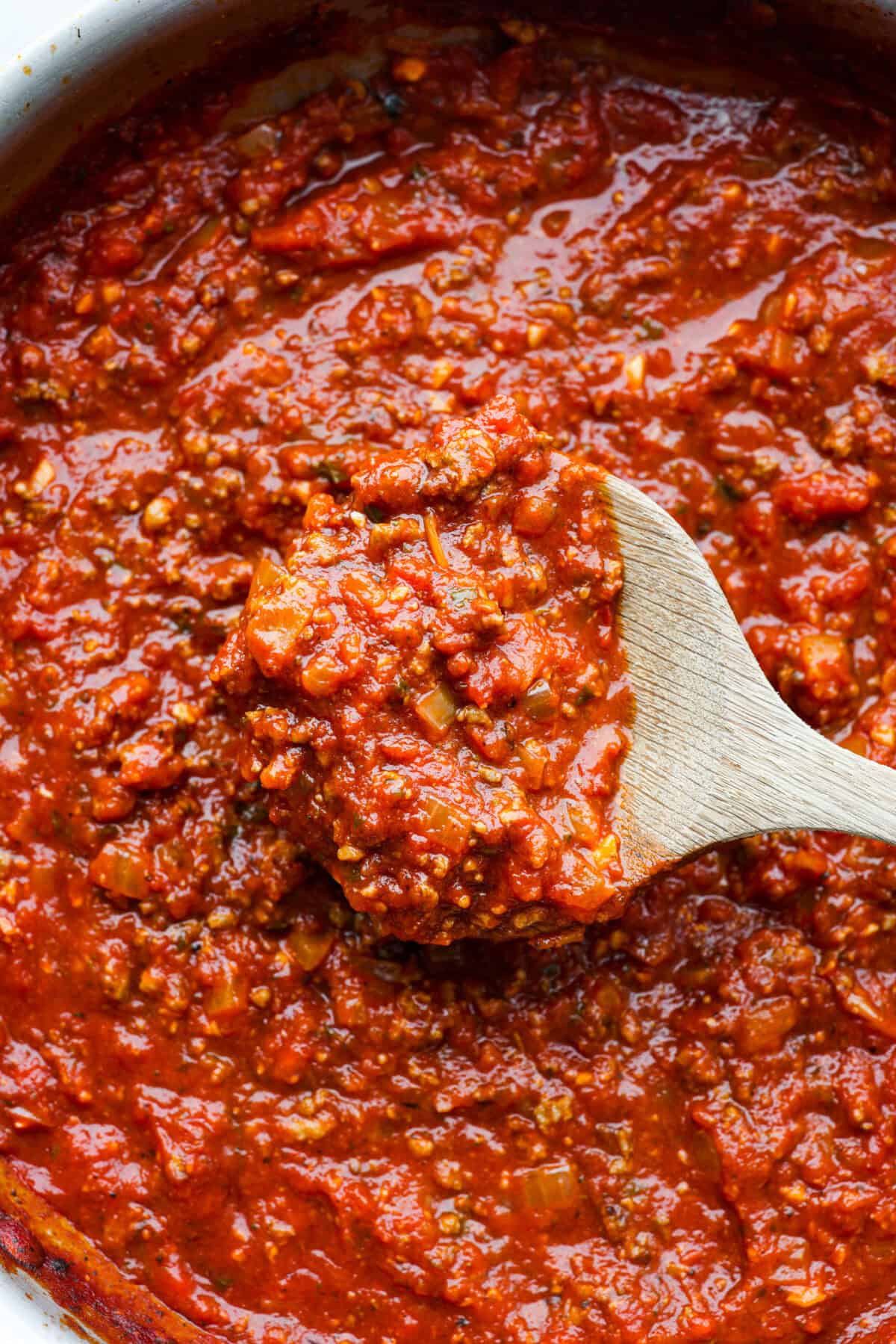 Close view of a wood spoon lifting up homemade spaghetti sauce.