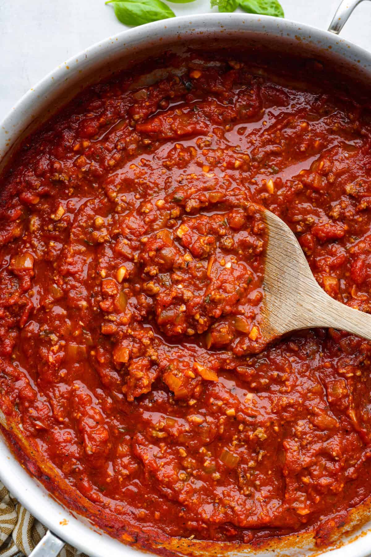 Top close view of homemade spaghetti sauce in a silver pan with a wood spoon.