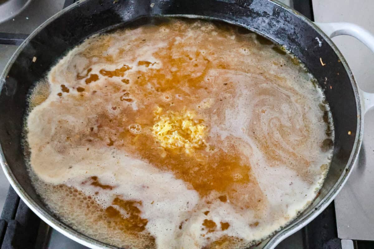 Angle shot of orzo pasta with liquid and lemon zest in a pan. 