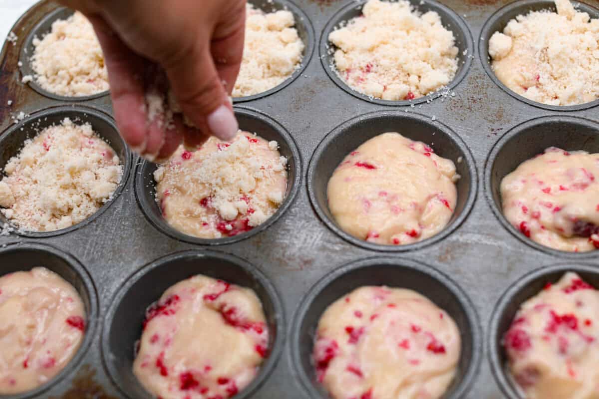 Angle shot of someone sprinkling streusel over muffin batter in muffin tin. 