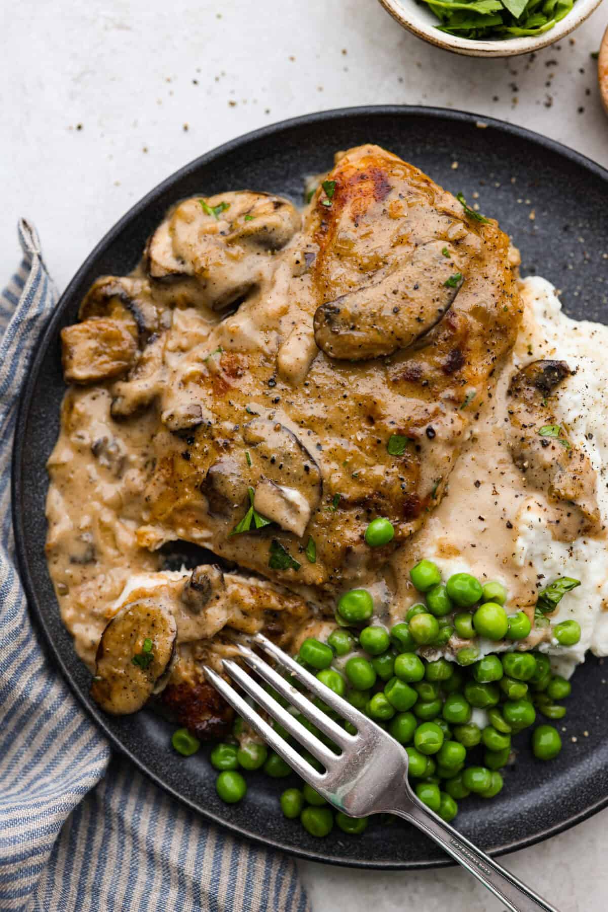 Overhead shot of plated smothered chicken over mashed potatoes and a side of peas. 