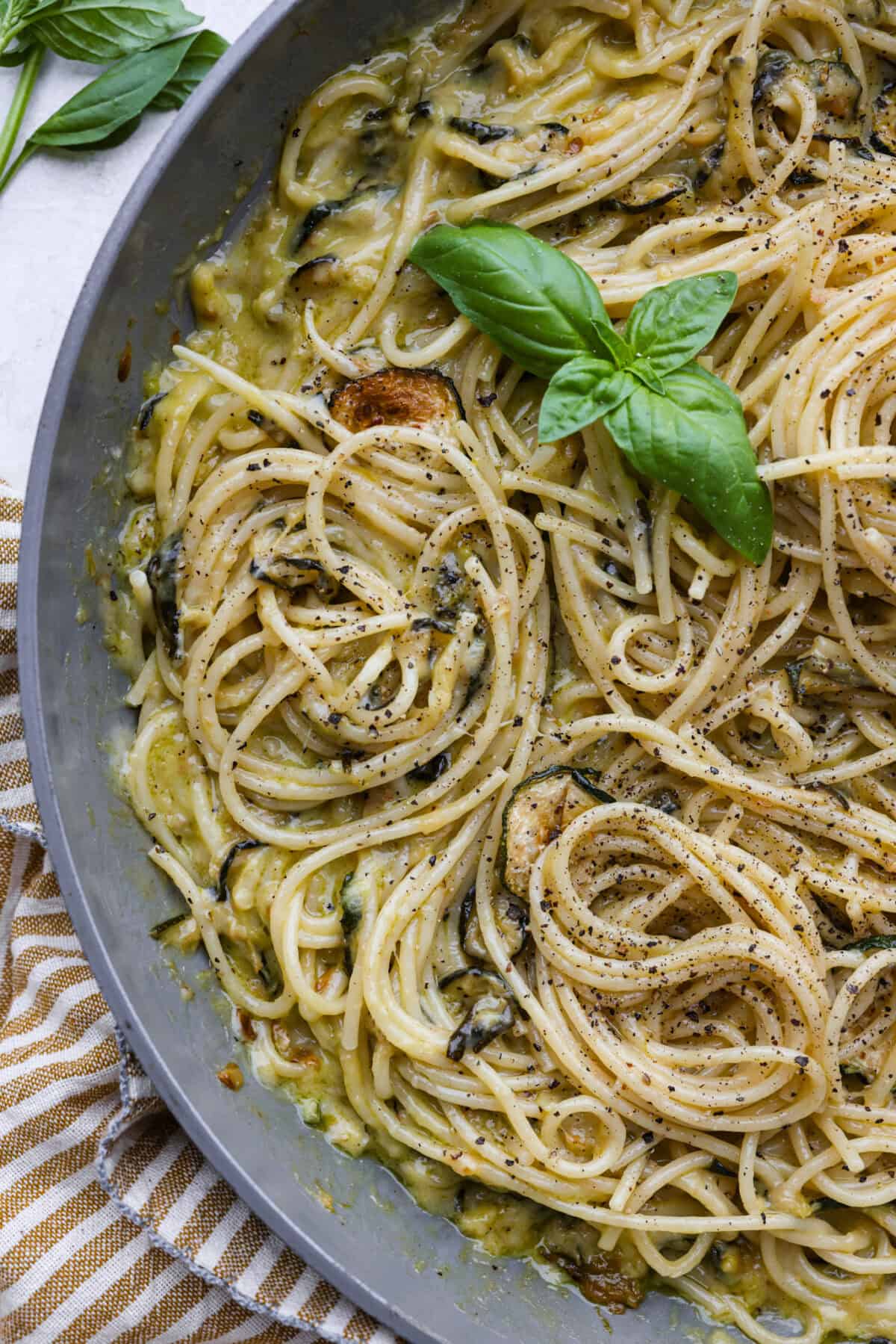 Close view of the spaghetti alla Nerano in a skillet garnished with fresh basil leaves.