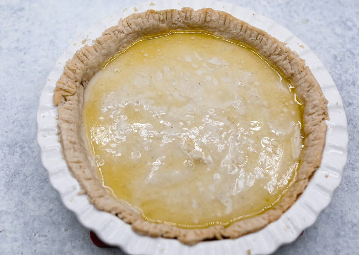 Overhead shot of pie crust in pie pan, filled with pie filling, with melted butter over the top. 