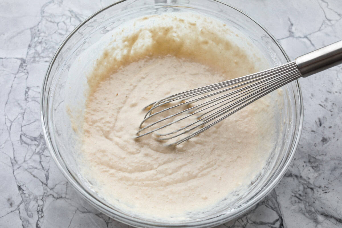 Overhead shot of wet and dry ingredients for zeppoles all mixed together in a bowl with a whisk. 