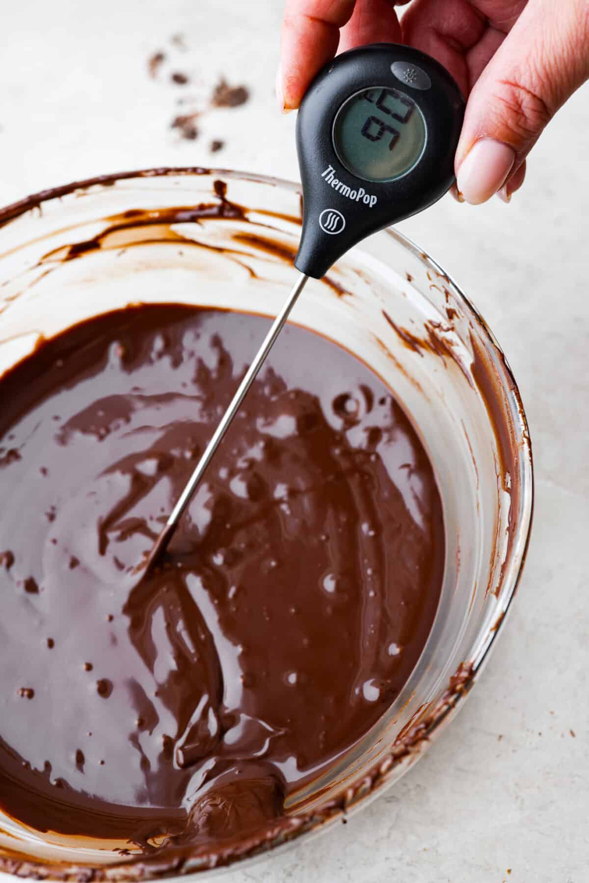 Close view of a thermometer testing the temperature of a bowl of melted chocolate.