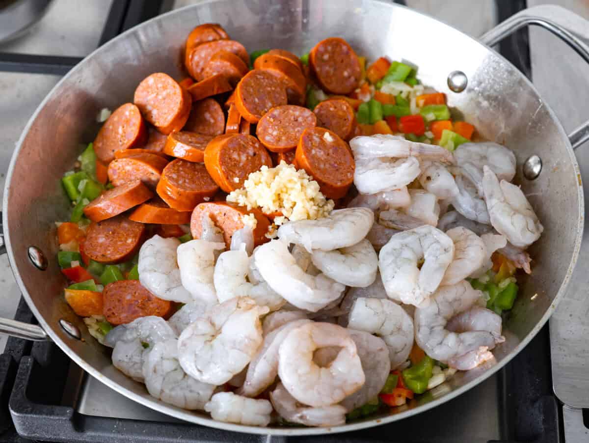 Overhead shot of sausage and shrimp added to the sautéing veggies in a skillet. 