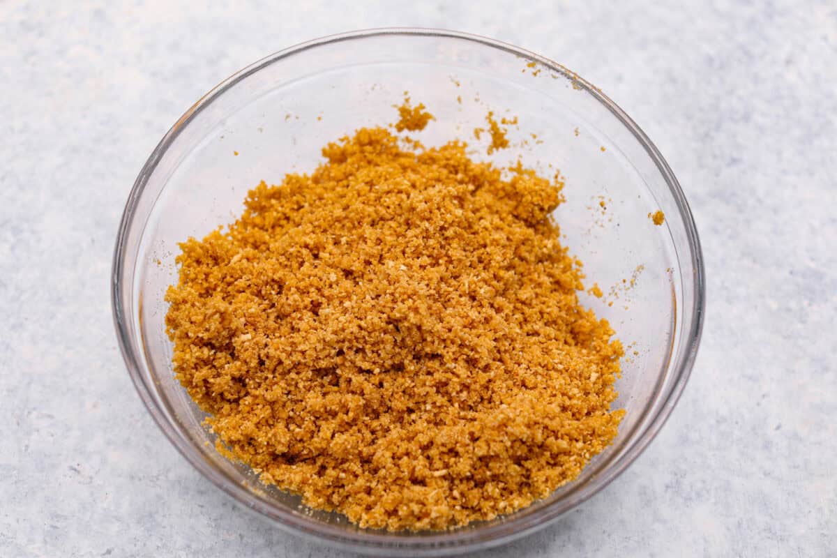 Overhead shot of graham cracker crust mixture in a glass bowl. 