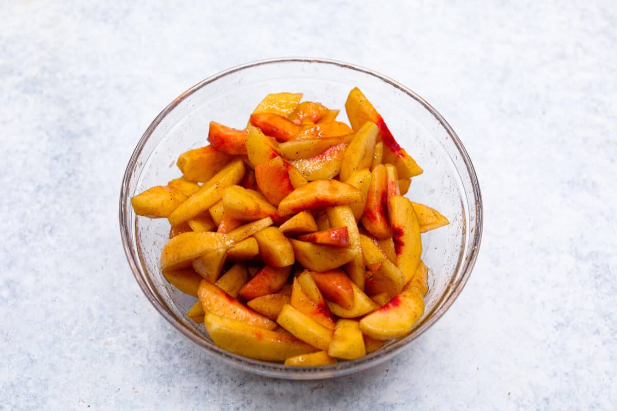 Overhead shot of the brown sugar, cinnamon, and nutmeg mixed in with the peaches in a glass bowl. 