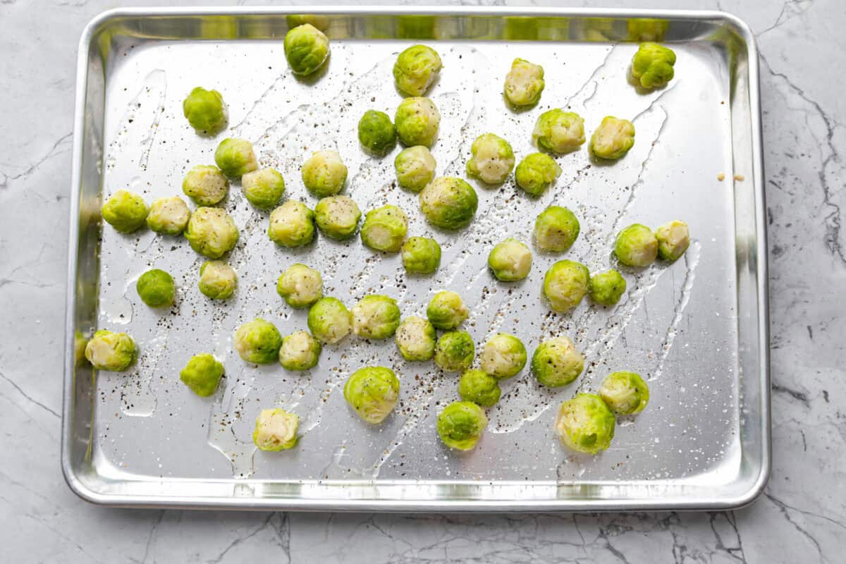 Overhead shot of boiled Brussels sprouts on a baking sheet drizzled with oil and sprinkled with salt and pepper. 