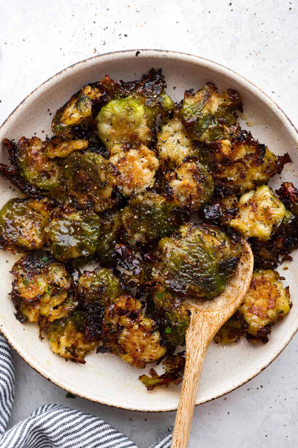 Overhead shot of smashed Brussels sprouts on a plate with a wooden serving spoon. 