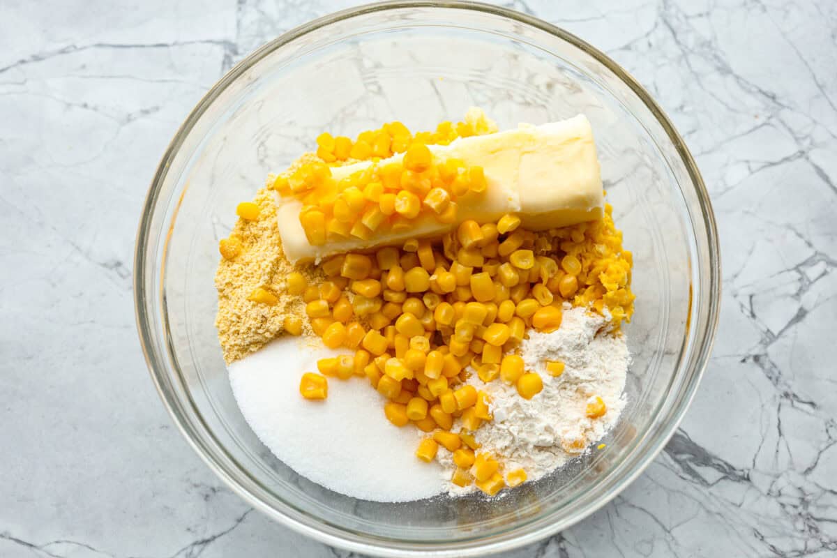 Overhead shot of pulverized corn, whole corn, flours, sugar, butter, and salt in a glass bowl. 