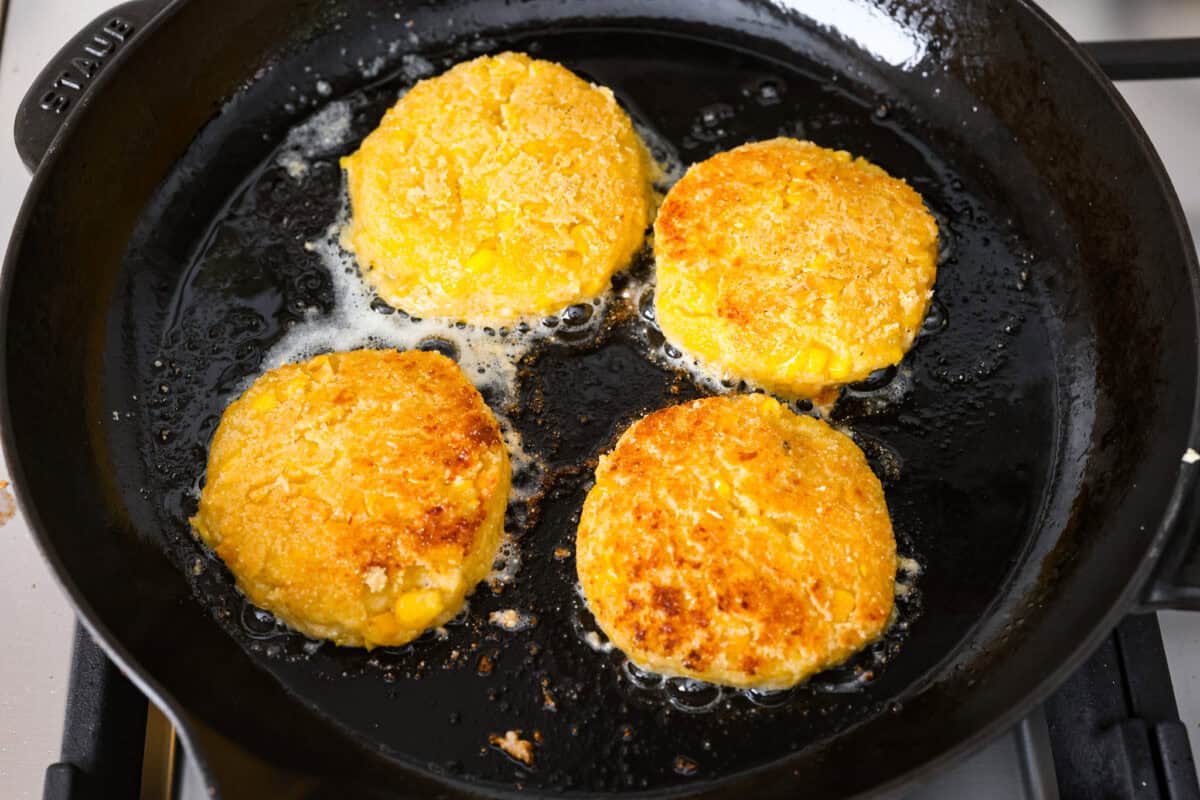 Overhead shot of corn cakes frying in oil on a skillet. 