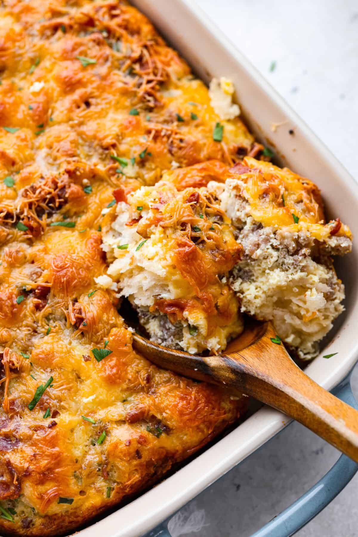 Close up shot of bubble up breakfast casserole in a baking dish with a wooden serving spoon. 