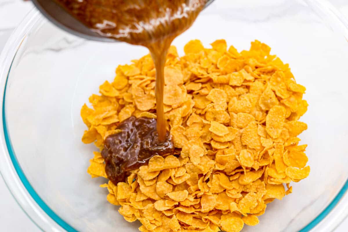 Overhead shot of someone pouring the boiled butter and sugar mixture over a bowl full of cornflakes. 