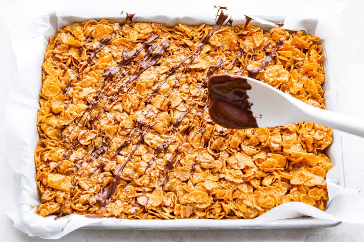 Overhead shot of someone drizzling chocolate over the cornflake and caramel mixture. 