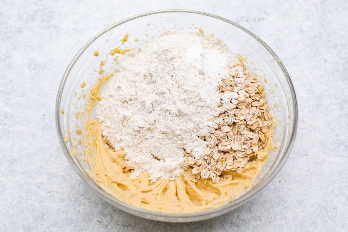 Overhead shot of butter mixture with oats, flour, baking powder, baking soda and salt on top. 