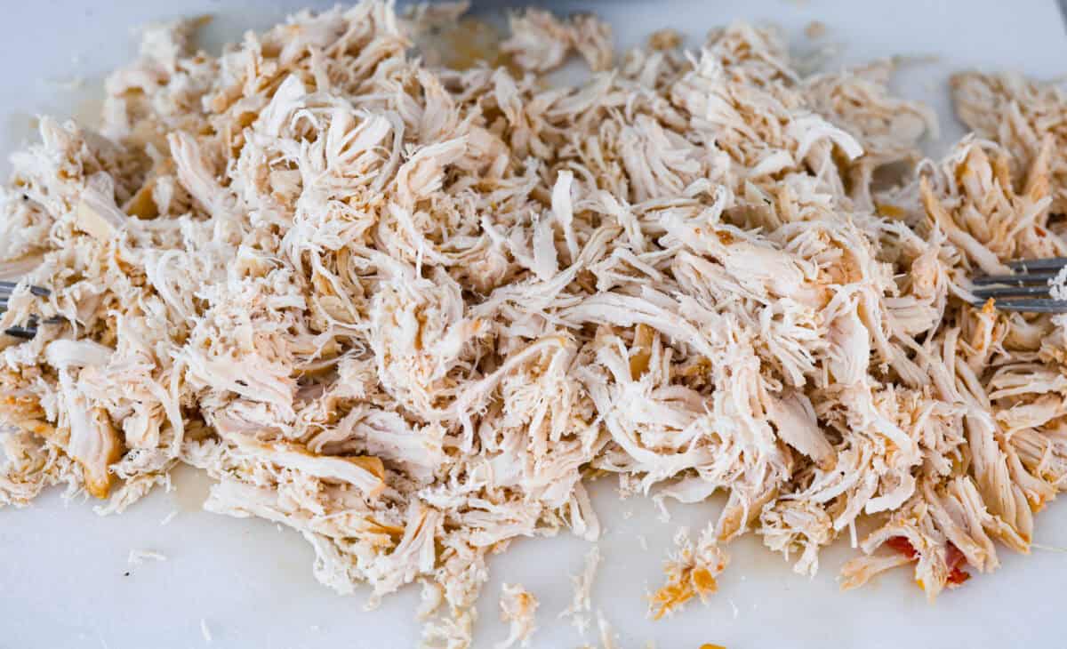 Angle shot of chicken shredded on a cutting board.