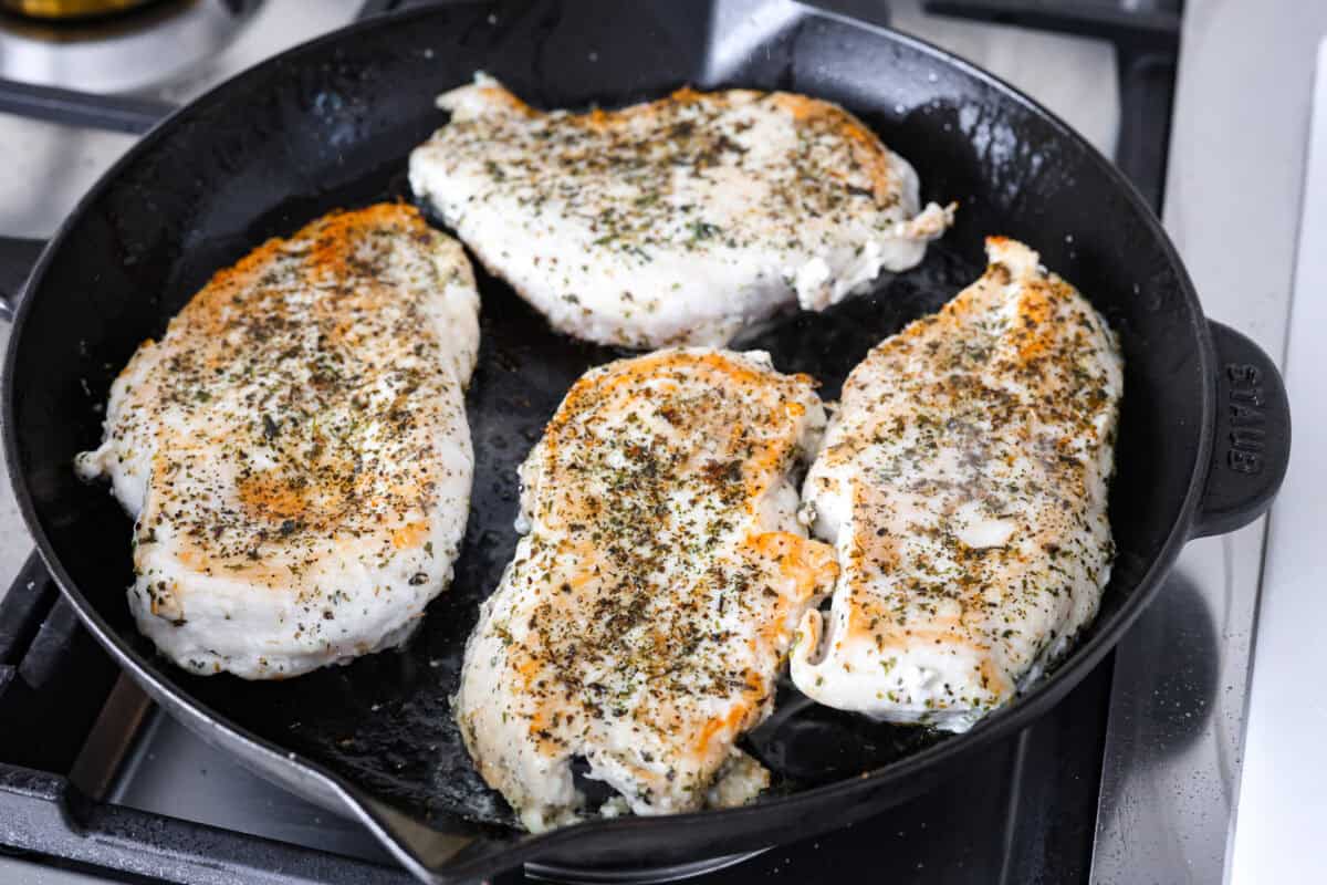 Angle shot of chicken breast searing in a skillet.