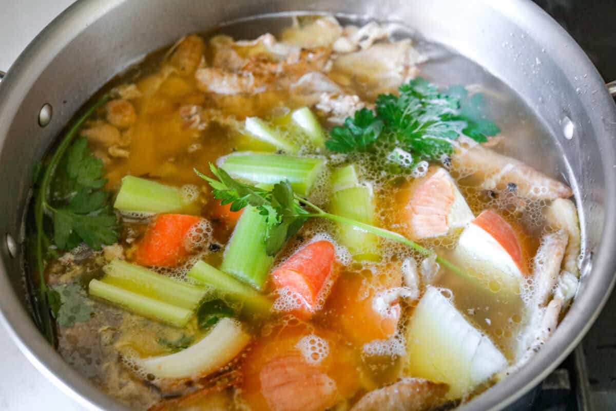 Angle shot of vegetables and herbs in the pot of water and bones simmering. 