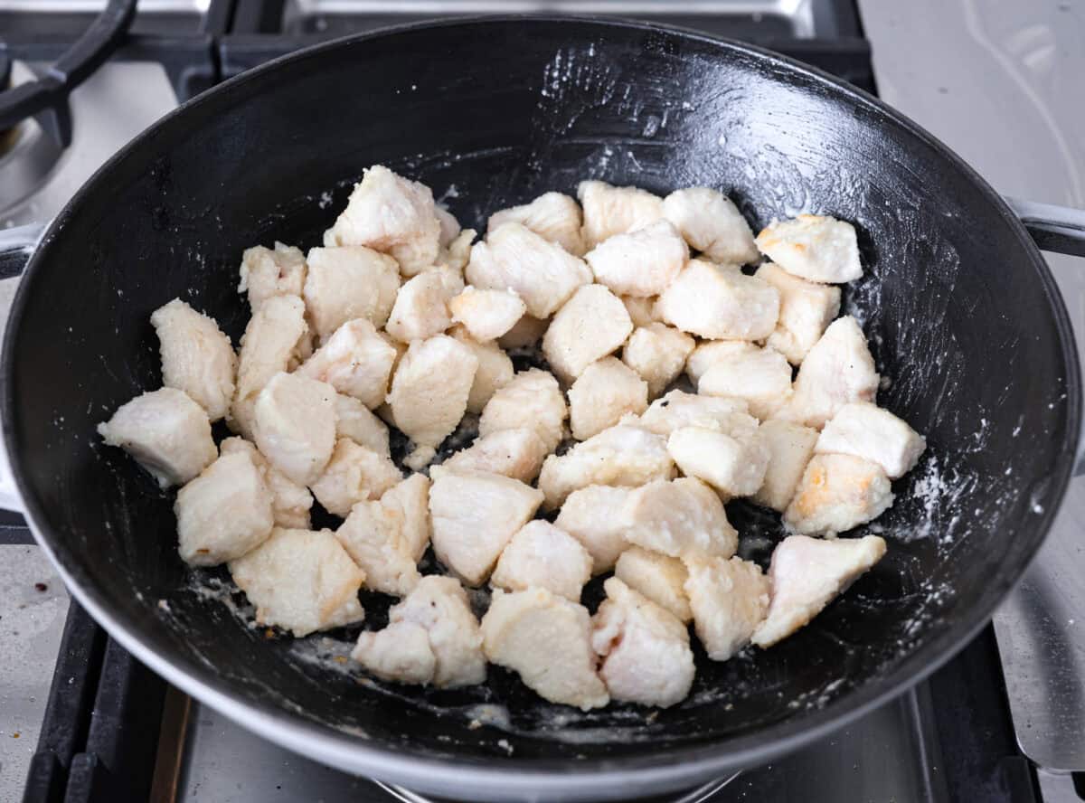 Angle shot of the chicken being cooked in a skillet on the stove top. 