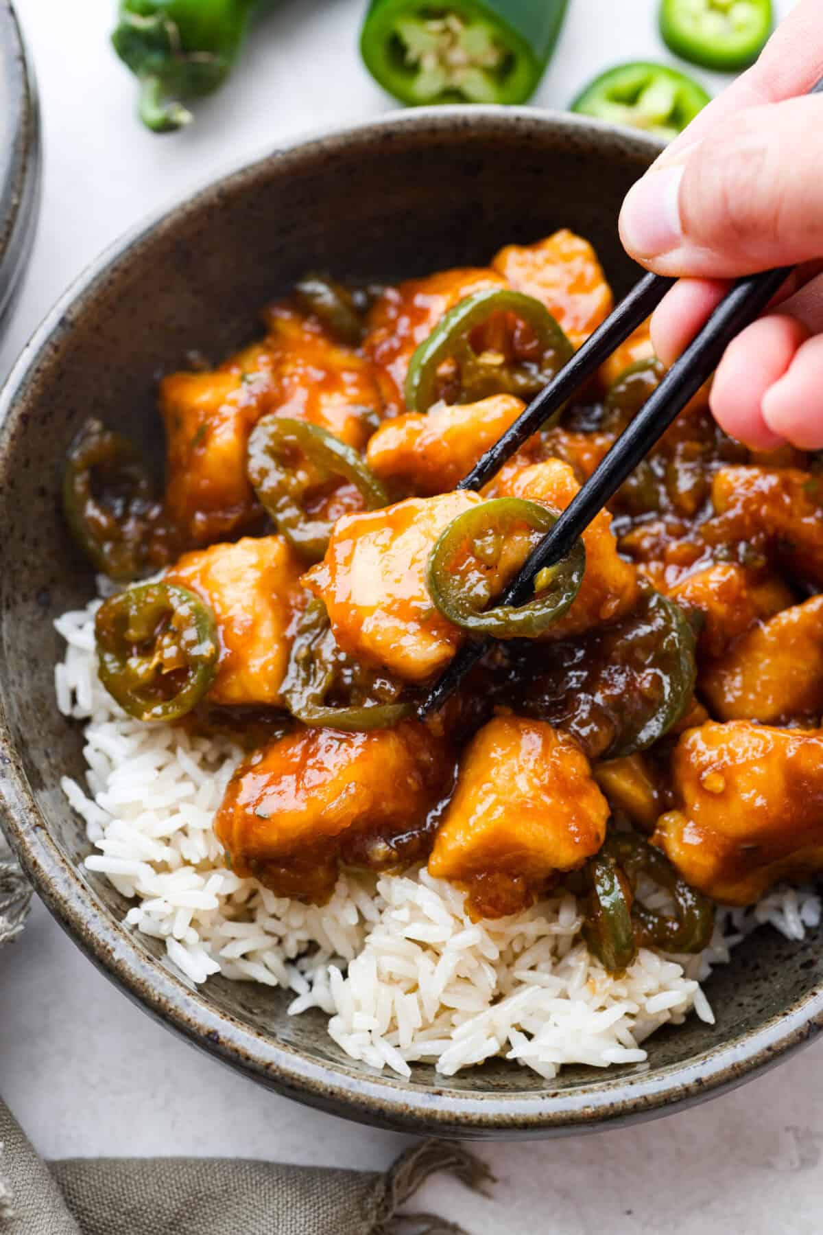 Close up shot of someone using chopsticks to get a bite of the plated jalapeño chicken. 