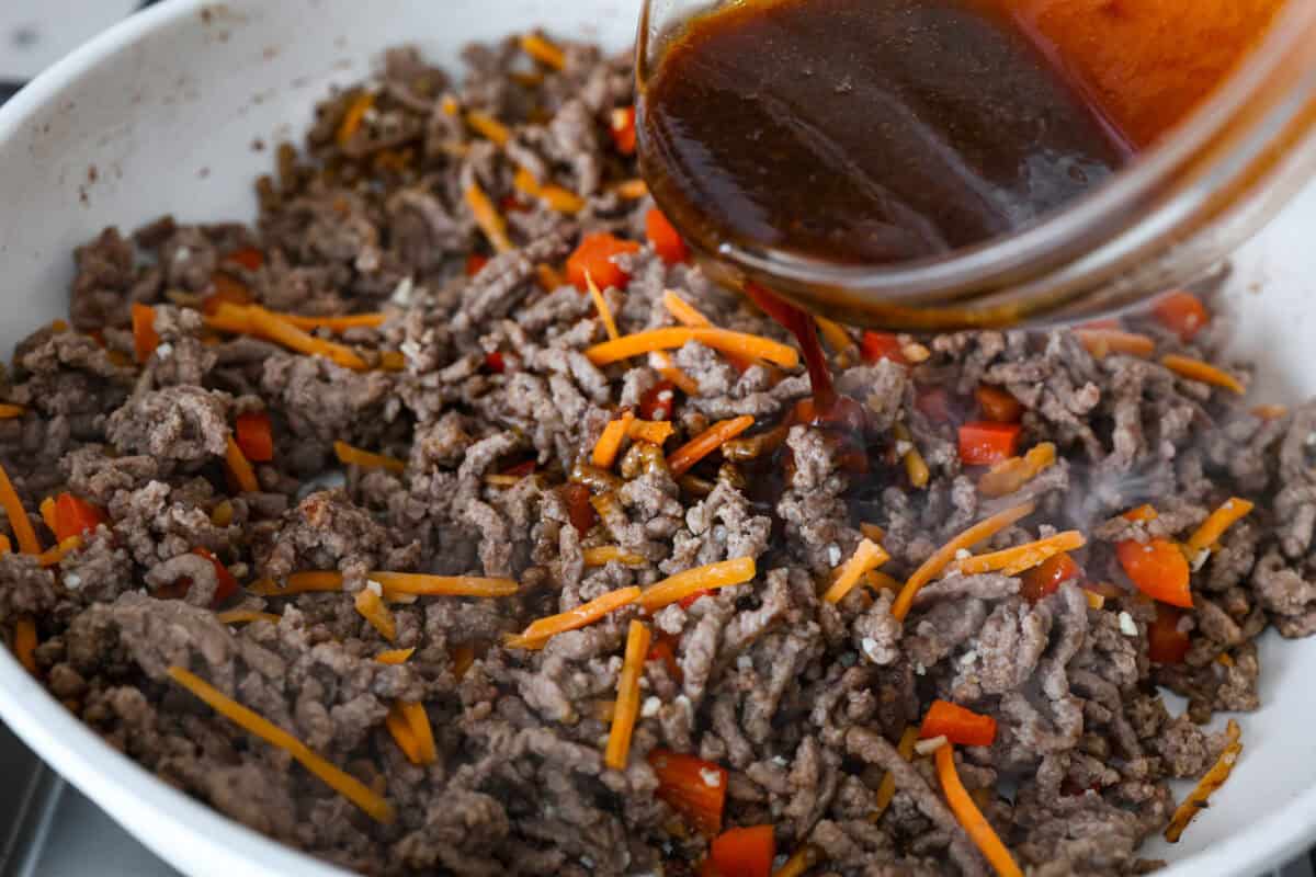 Angle shot of sauce being poured over meat and vegetable mixture. 