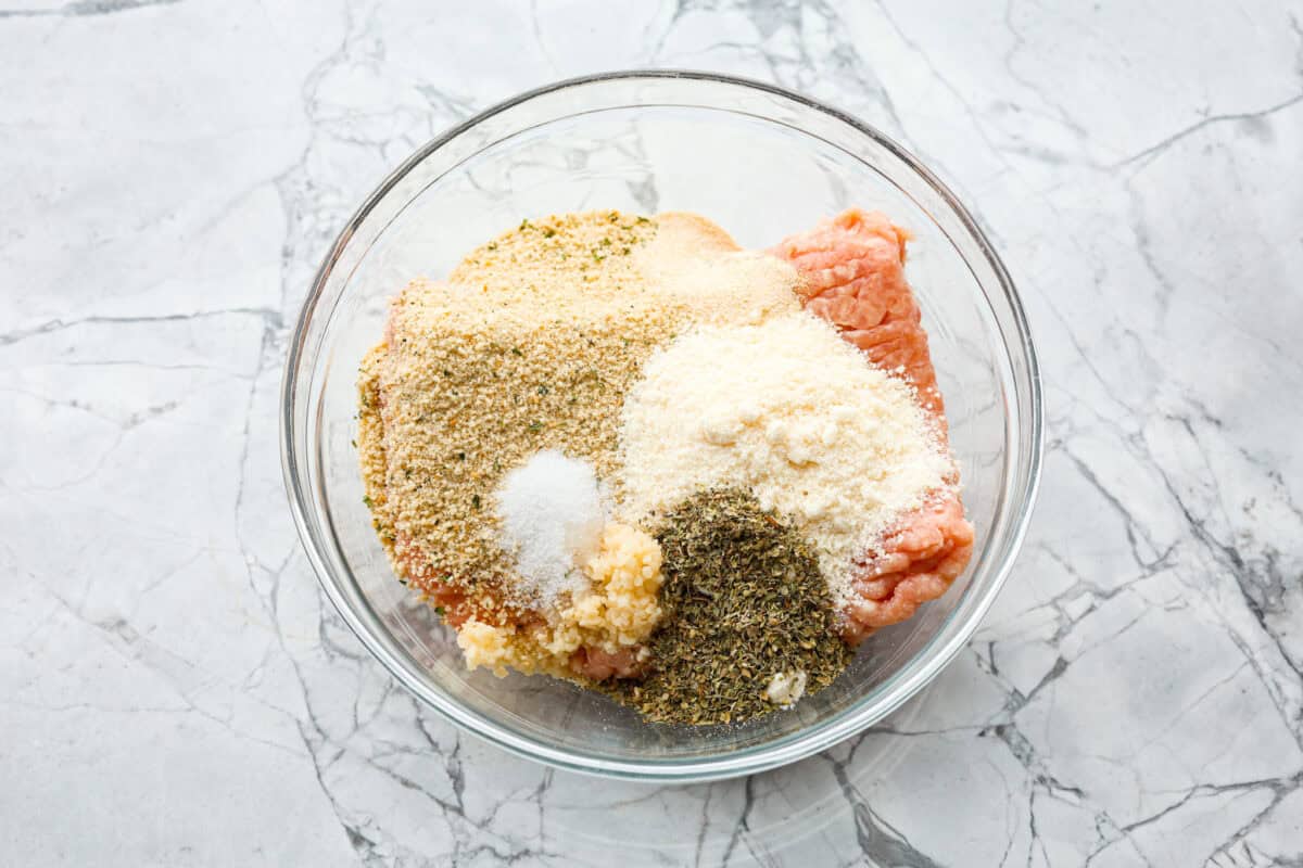 Overhead shot of meatball ingredients dumped in a glass bowl. 