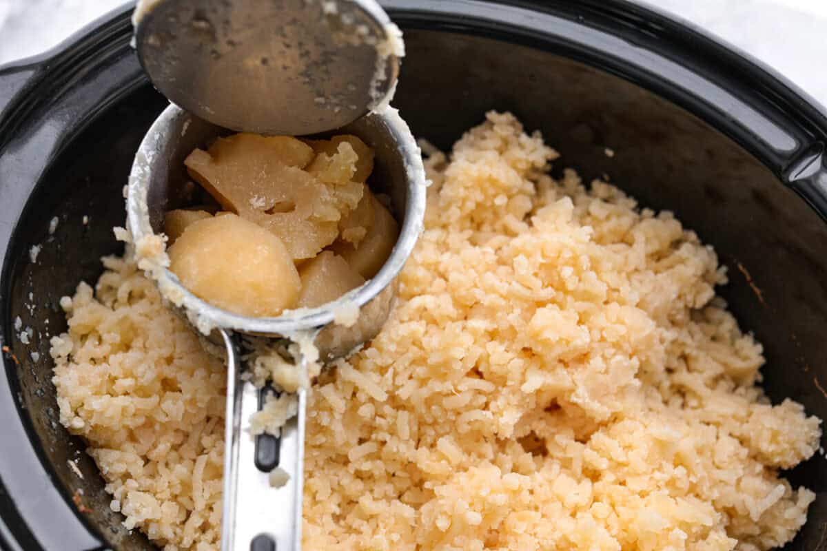 Overhead shot of someone mashing potatoes into the crock pot. 