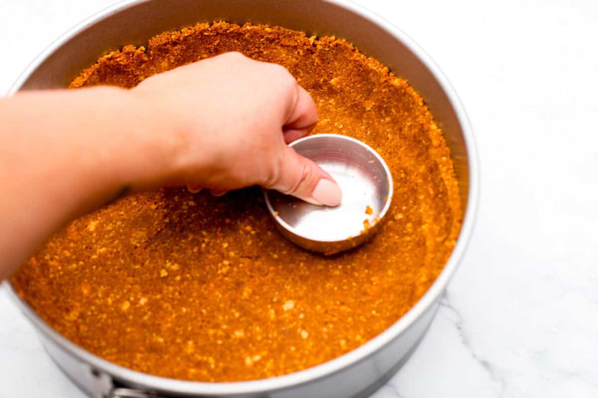 Overhead shot of someone smashing the crust mix into the bottom of a spring form pan. 