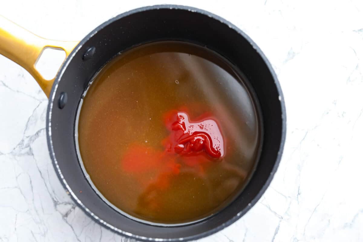 Overhead shot of pineapple juice, vinegar, brown sugar, ketchup, and soy sauce, in a sauce pan. 