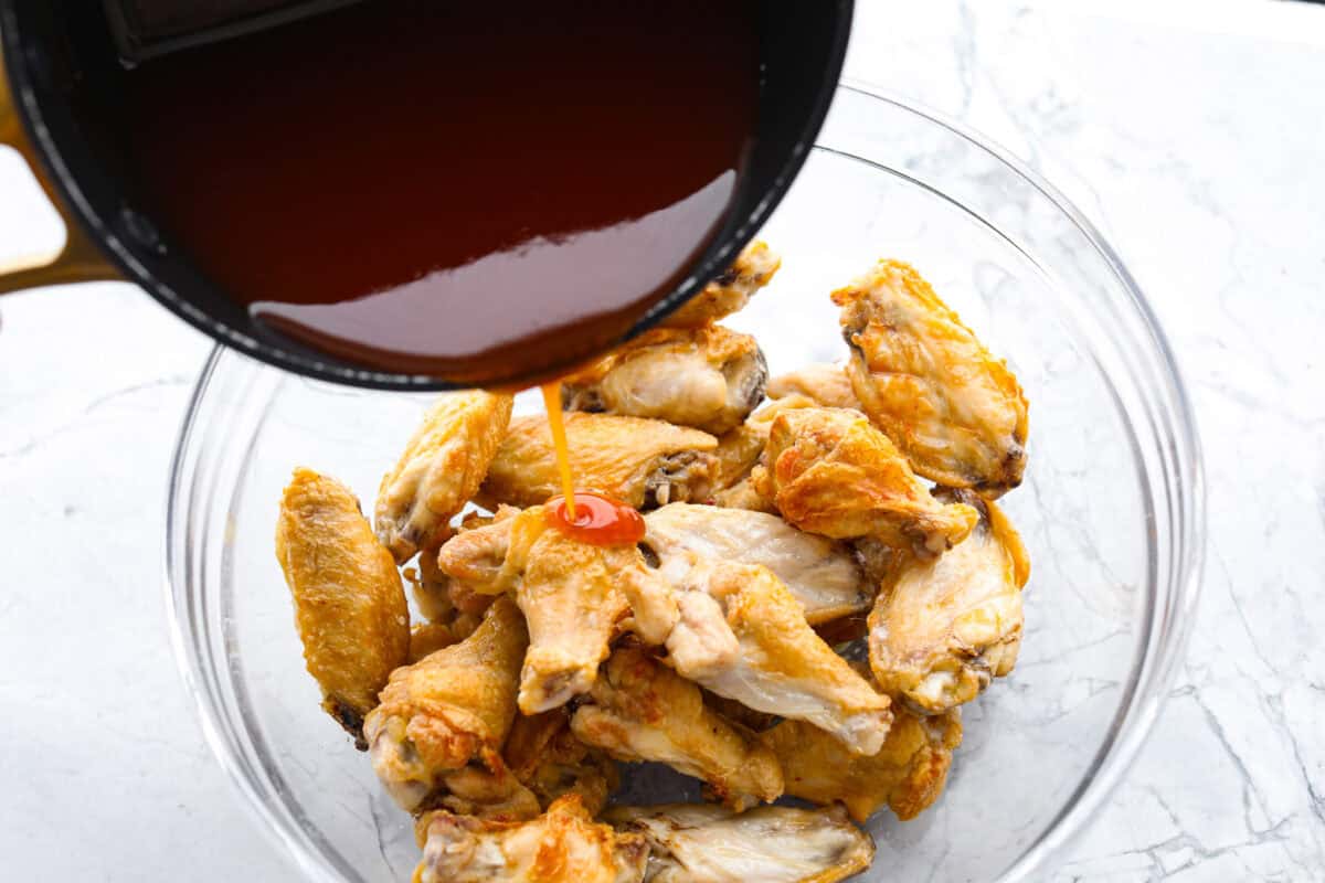 Angle shot of someone pouring sweet and sour sauce over baked chicken wings. 