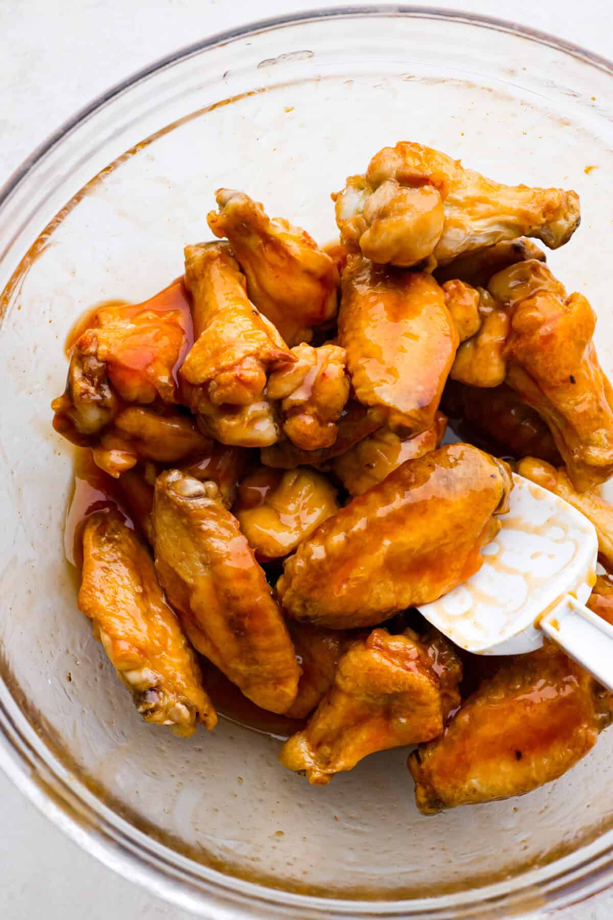 Close up shot of someone stirring wings covered in sweet and sour sauce in a glass bowl. 