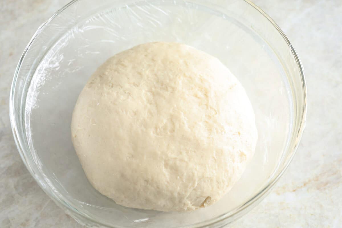 Overhead shot of a bao bun dough ball in the bottom of an oiled glass bowl. 