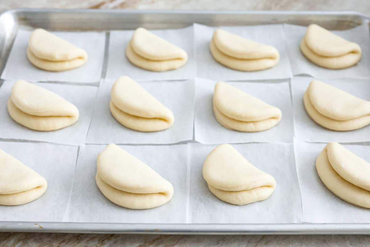 Angle shot of boa bun circles folded in half on parchment paper on a baking sheet. 