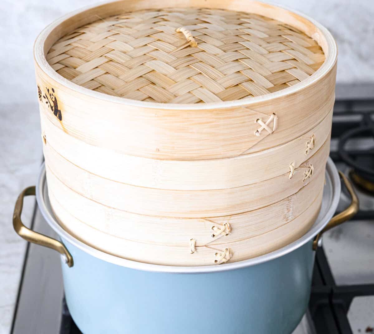 Side shot of pot with boiling water, fitted with a steam ring and a bamboo steam on top.