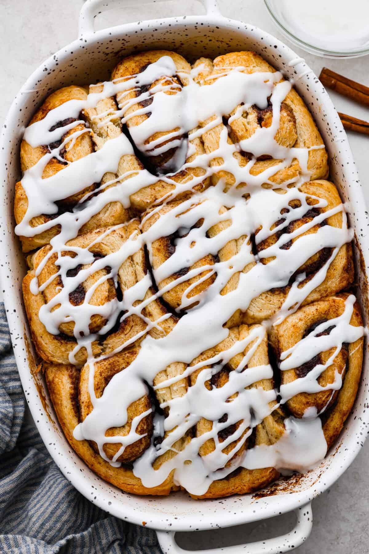 Overhead shot of biscuit cinnamon rolls in a baking dish drizzled with glaze.