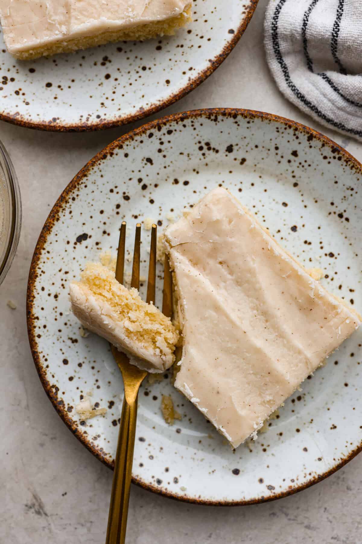 Close up shot of a plated peice of browned butter sheet cake with a bite taken out with a gold fork.