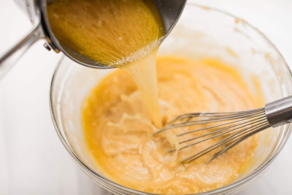 Angle shot of someone pouring the water and browned butter into the dry ingredients while whisking. 