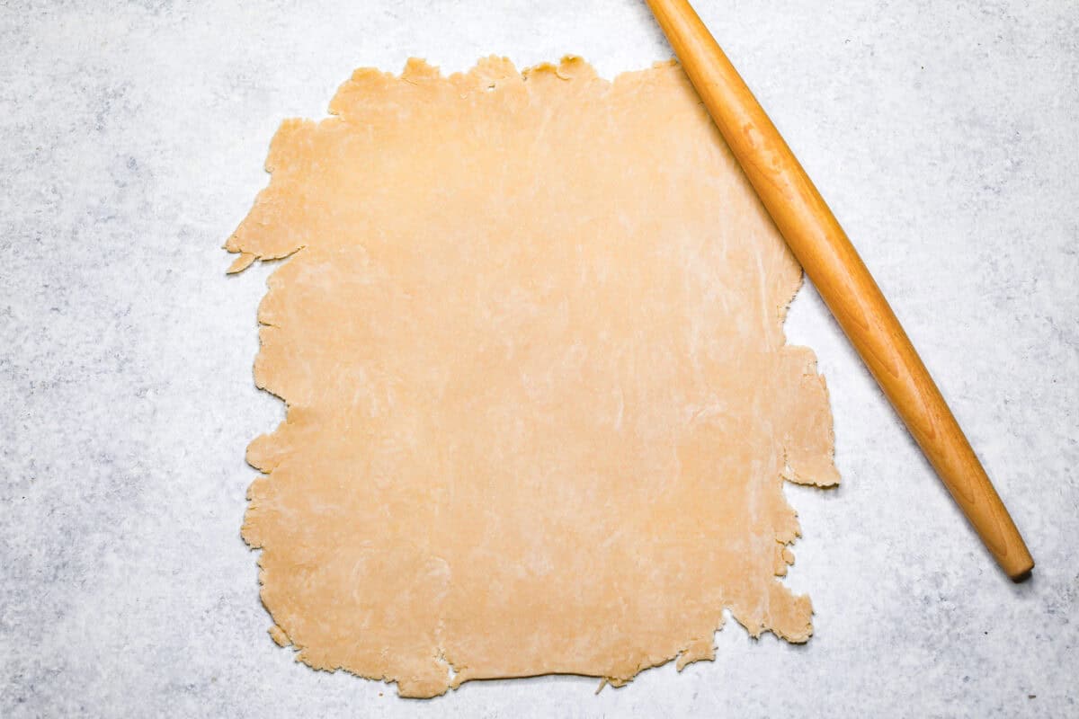 Overhead shot of pie crust rolled into a rectangle with a rolling pin next to it. 