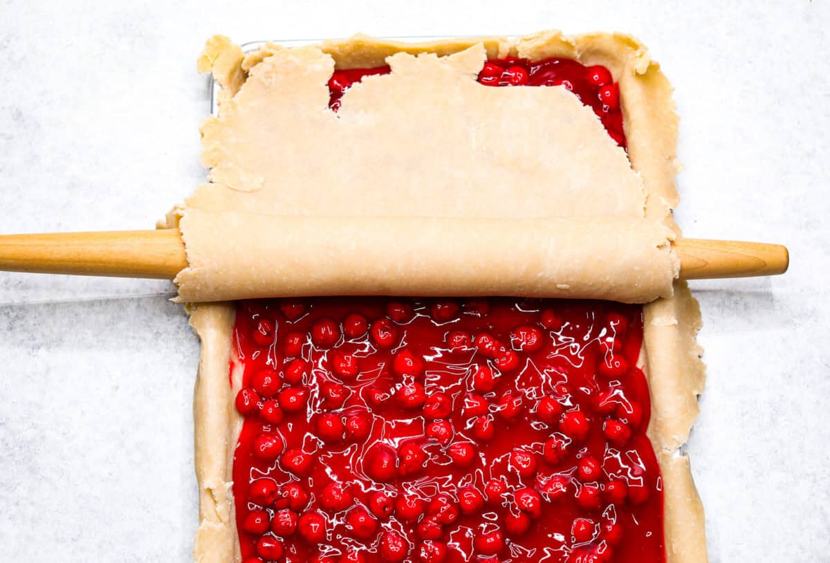 Overhead shot of the sheet pan with pie crust, pie filling and another layer of pie crust being rolled over the top. 