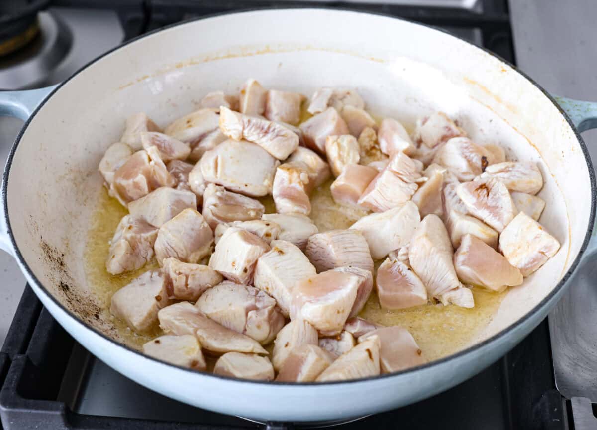 Angle shot of chicken being searing in oil and ghee in a skillet. 